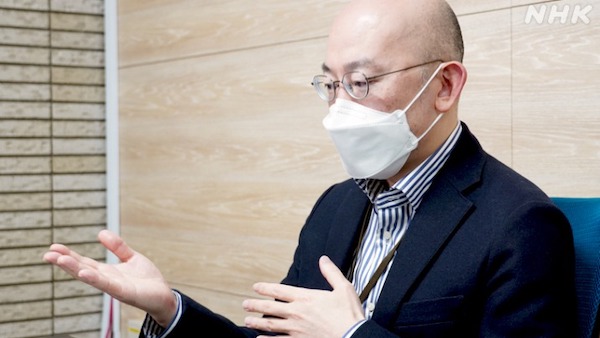 Asian male wearing a mask sitting at a desk